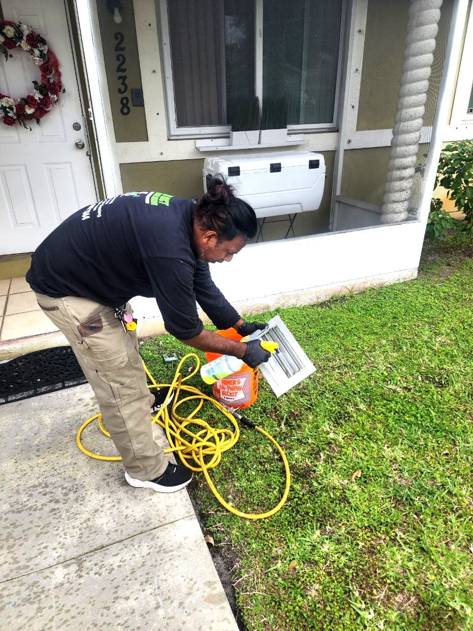 Technician cleaning AC vent covers outside the home